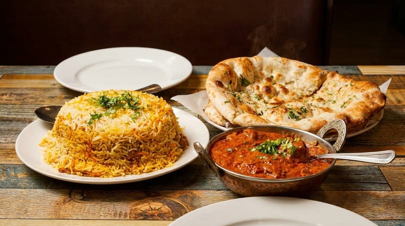 Indian biryani rice, naan bread, and chicken curry served on a rustic wooden table.