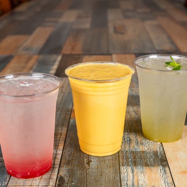 Three cold drinks: pink soda, yellow smoothie, and mint lemonade on a rustic wooden table.