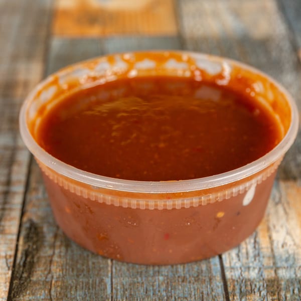Red salsa in a clear plastic takeout container on a wooden table.