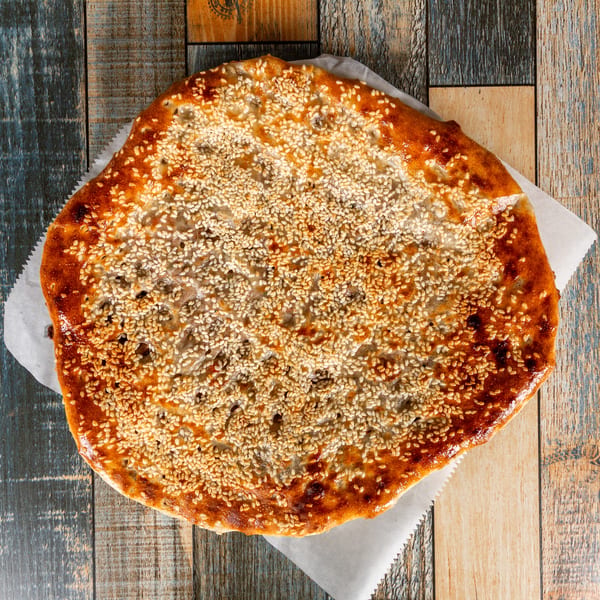 Golden brown flatbread covered in sesame seeds on a rustic wooden table.
