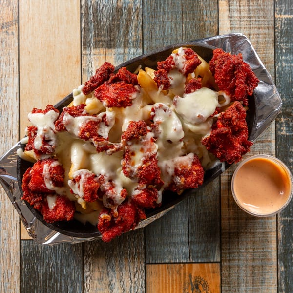 Fries topped with red crispy chicken pieces and melted white cheese, served with a side sauce.