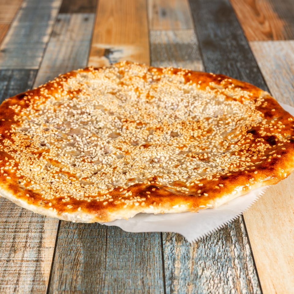 Golden brown sesame flatbread on white paper, on a rustic wooden table.